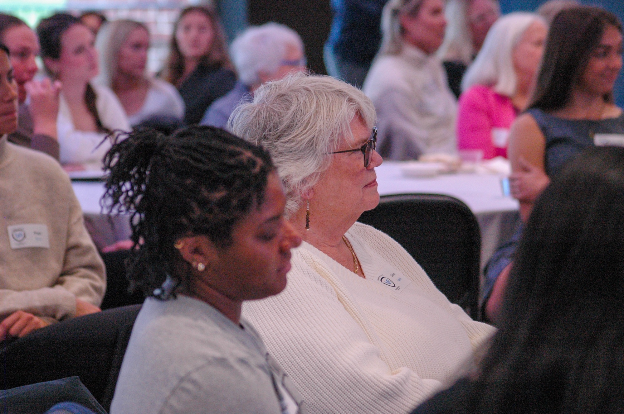 Students and alumnae gathered at a TFL PowHER Hour event, listening to a panel discussion on stage